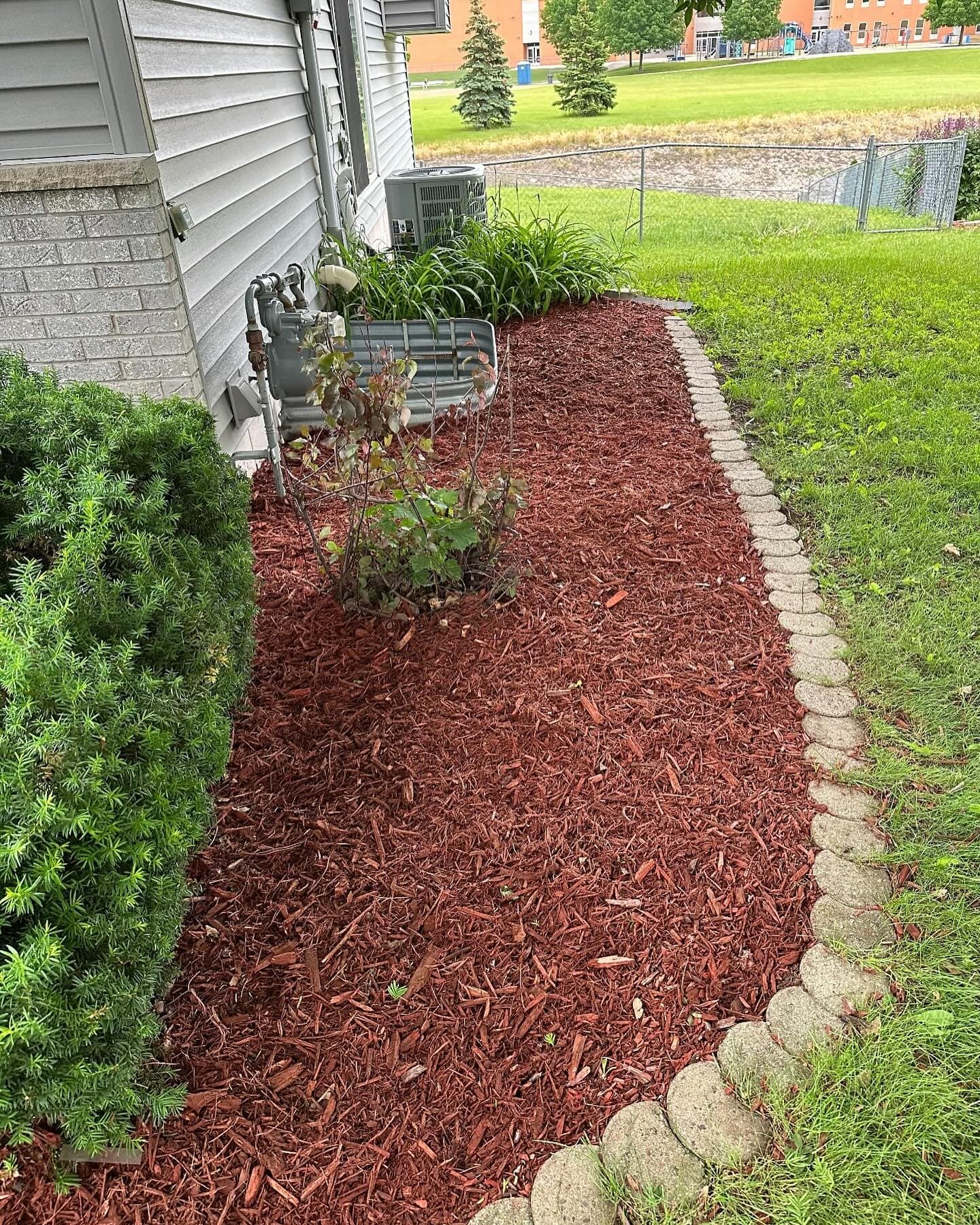 Red mulch landscaping around a home with decorative stone edging and shrubs.