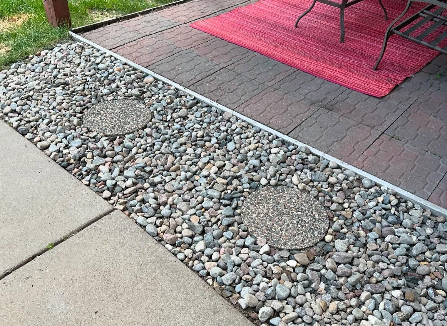 Patio area with pebbled landscaping and circular stepping stones next to a red rug and furniture.