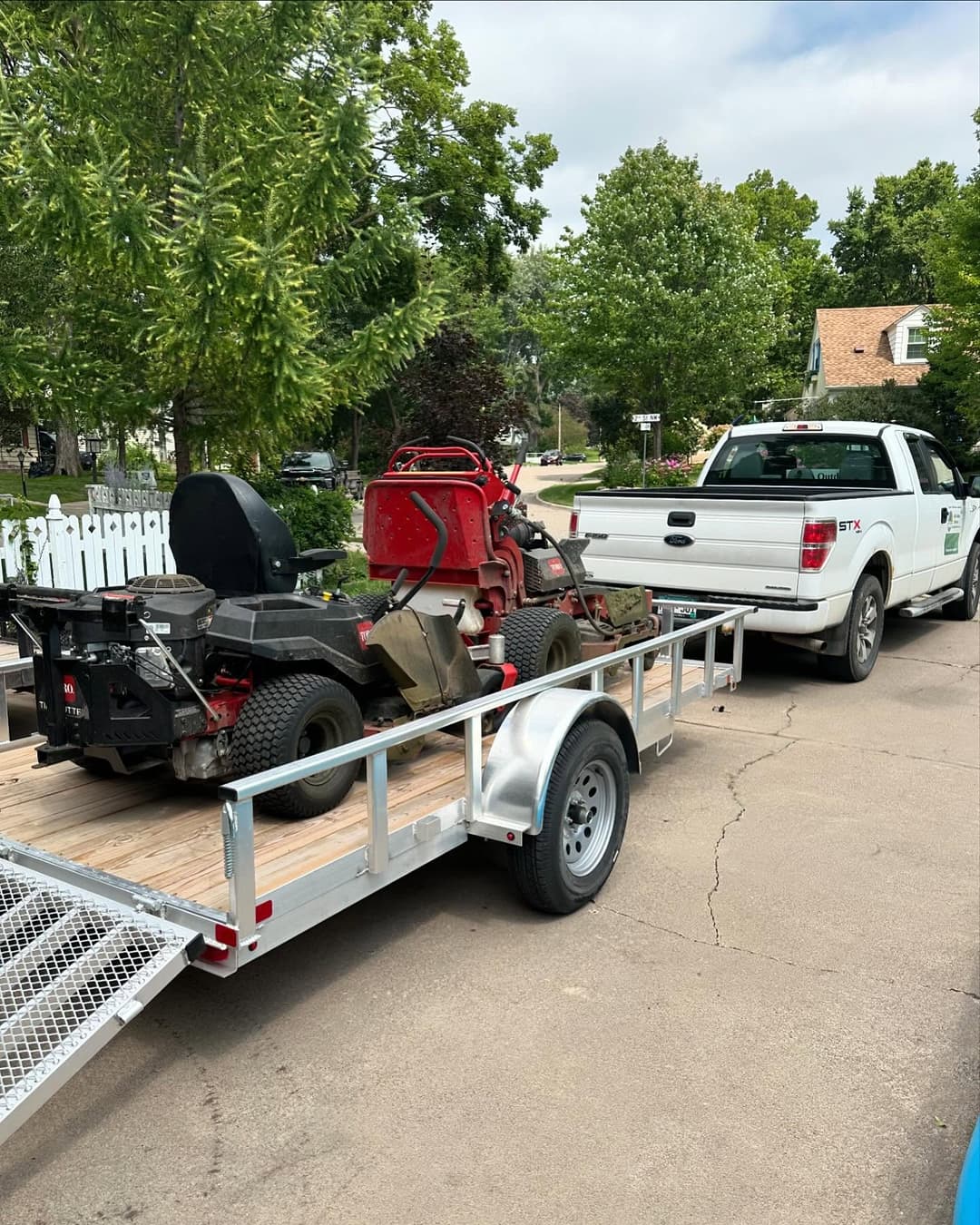 Pickup truck towing a trailer with lawn equipment parked on a residential street.