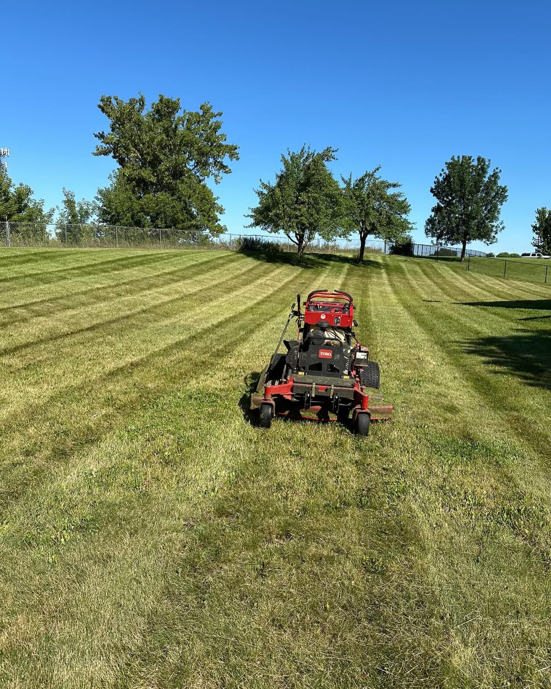 Lawn mower on freshly cut grass with clear blue sky and trees in background.