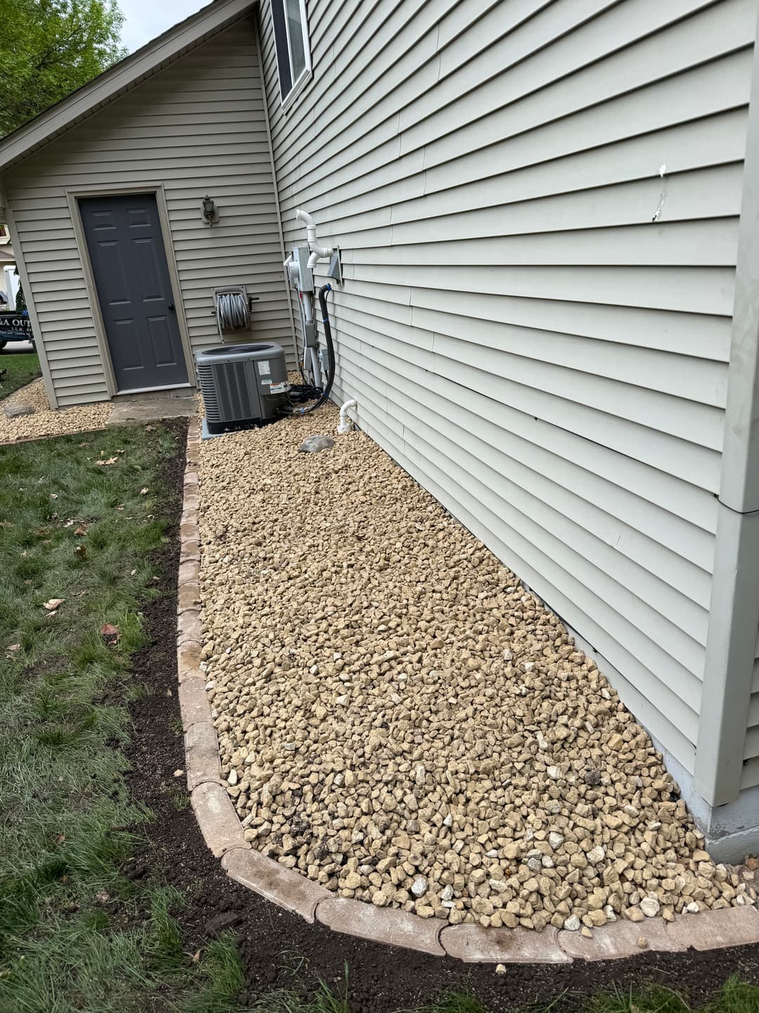 Gravel landscaping along a home's exterior with air conditioning unit and gray siding.