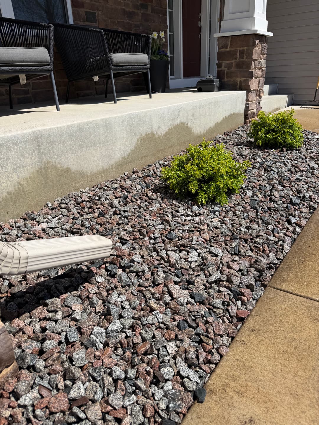 Landscaped front yard with stone gravel, shrubs, and porch seating area.