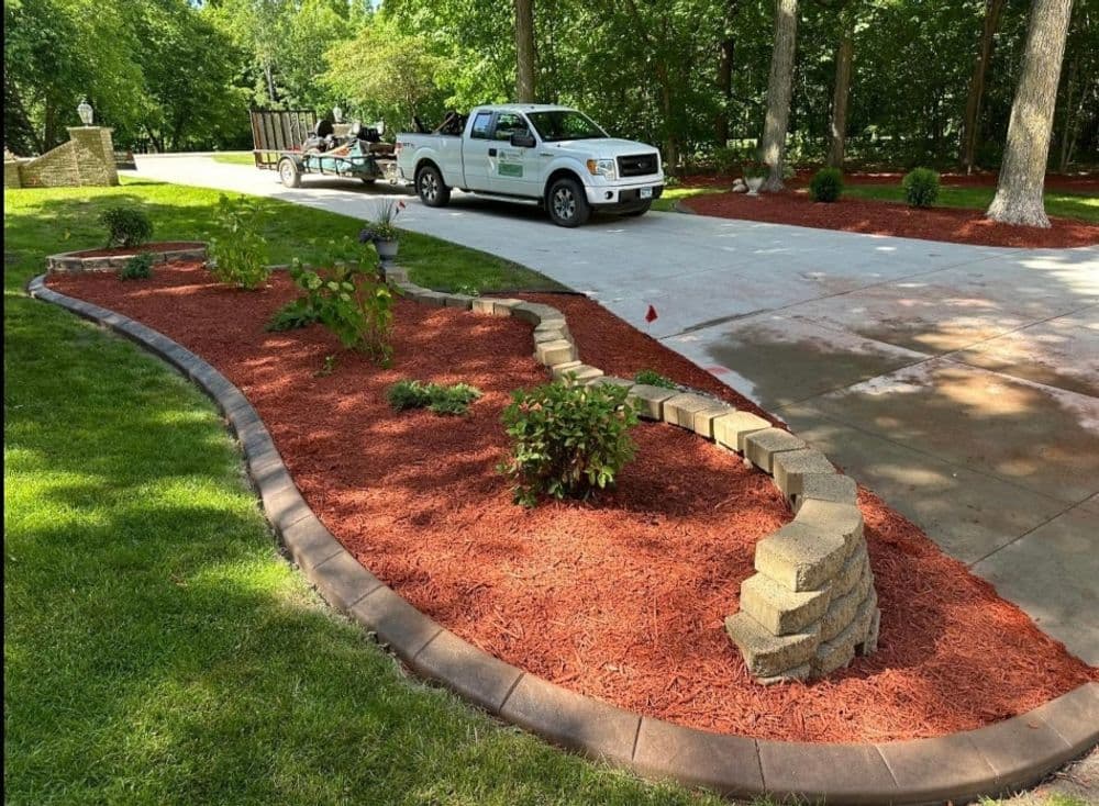 Well-landscaped garden with stone border and freshly laid mulch beside a parked truck.