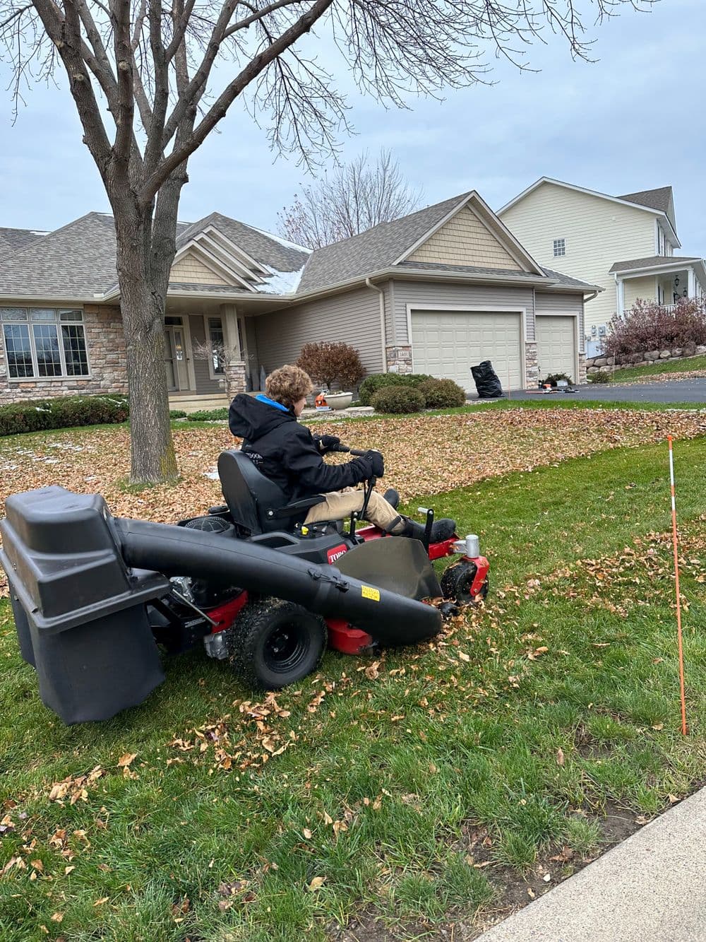 Person using a riding lawn mower to clear leaves from a residential yard in autumn.