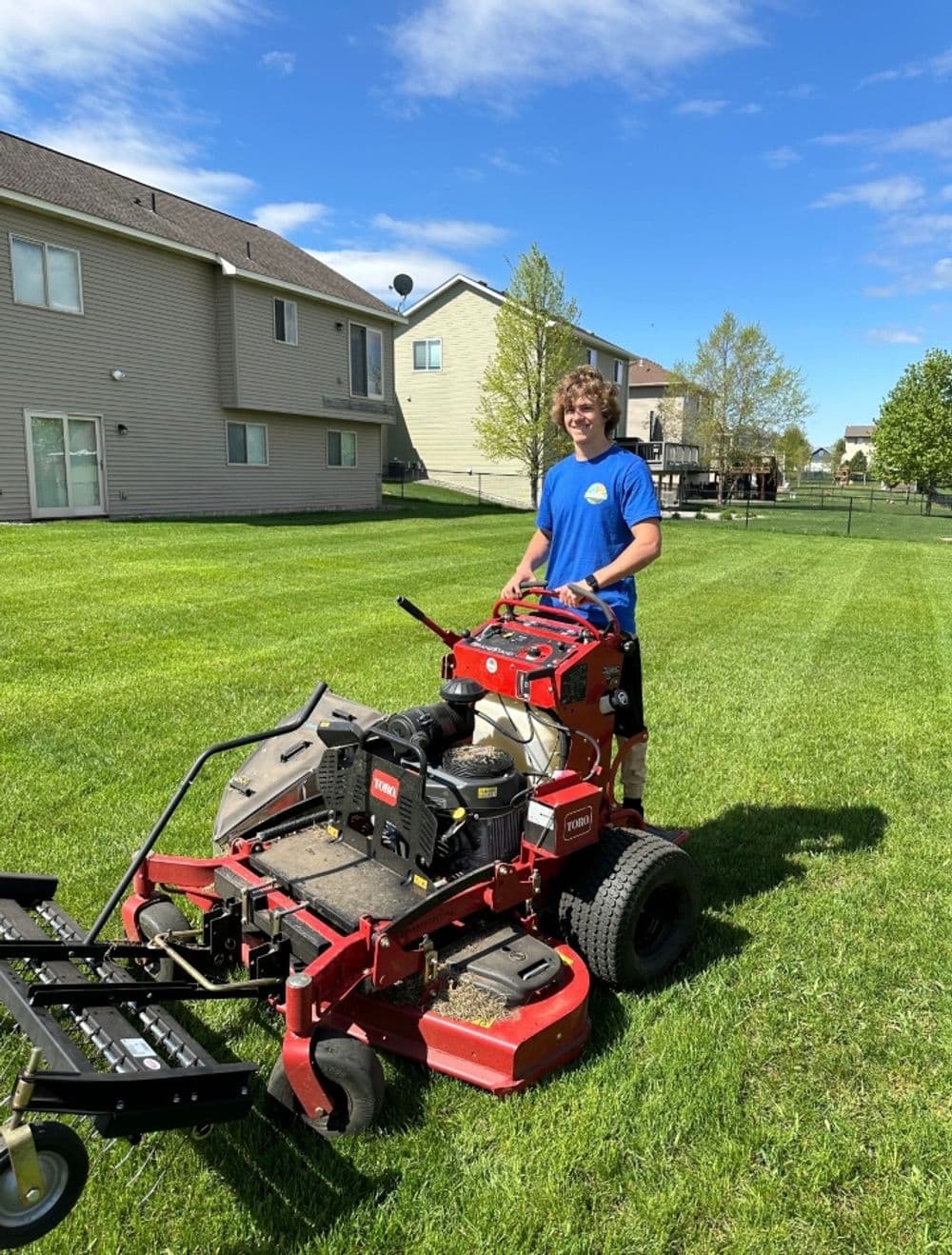 Lawn care professional operating a riding mower on a sunny residential lawn.