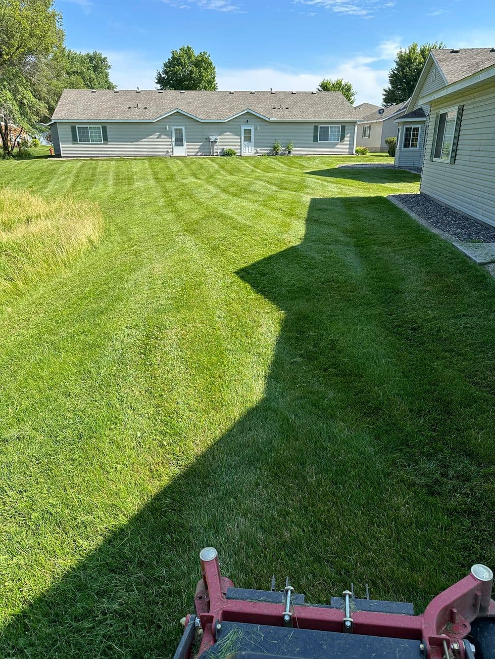 Lawn mowing in a well-maintained backyard with neat stripes and nearby houses.