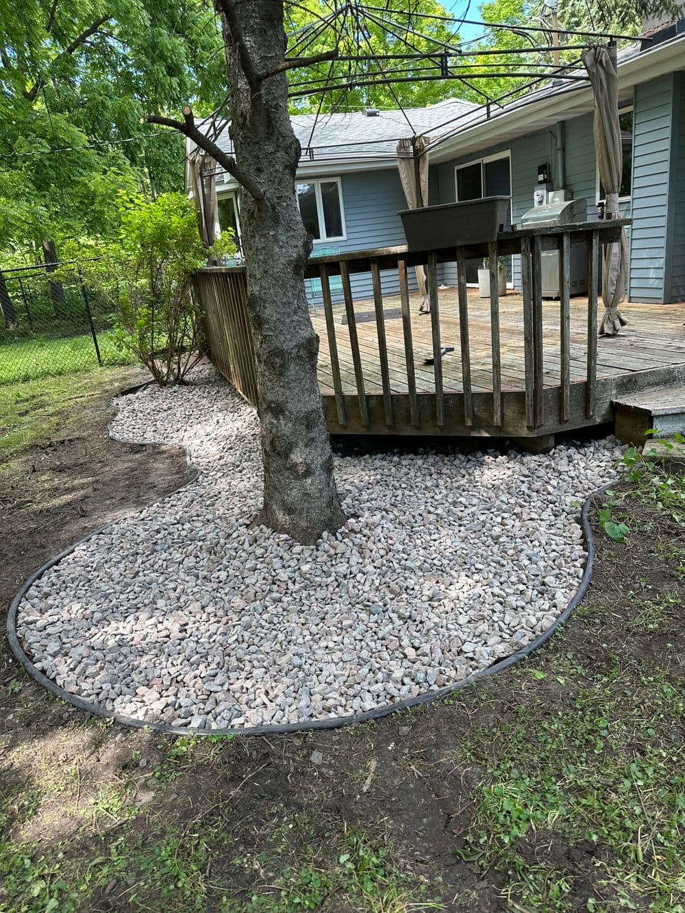 Landscape design featuring gravel around a tree base, complementing a wooden deck in a garden.