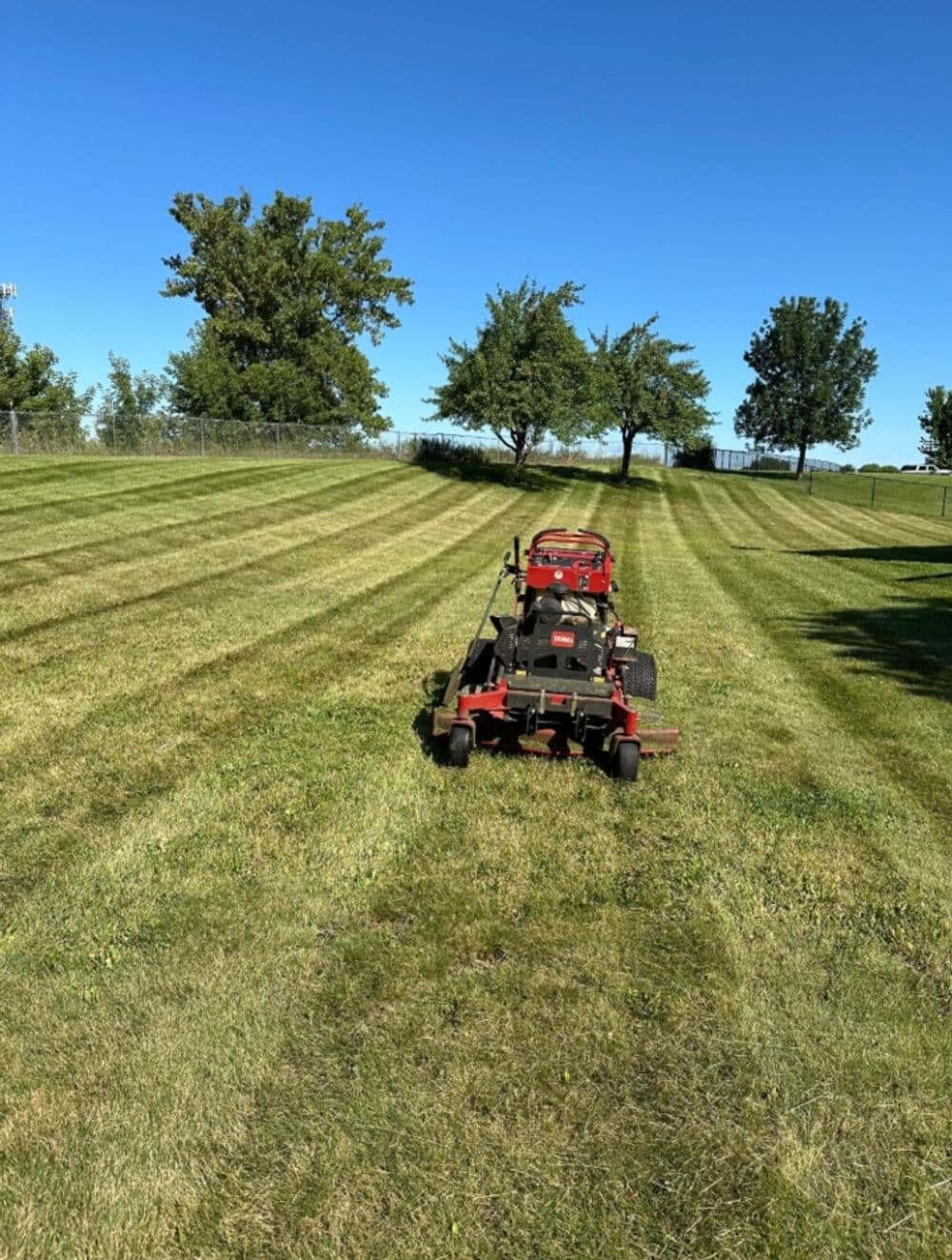 Lawn mower on freshly cut grass under a clear blue sky, with trees in the background.