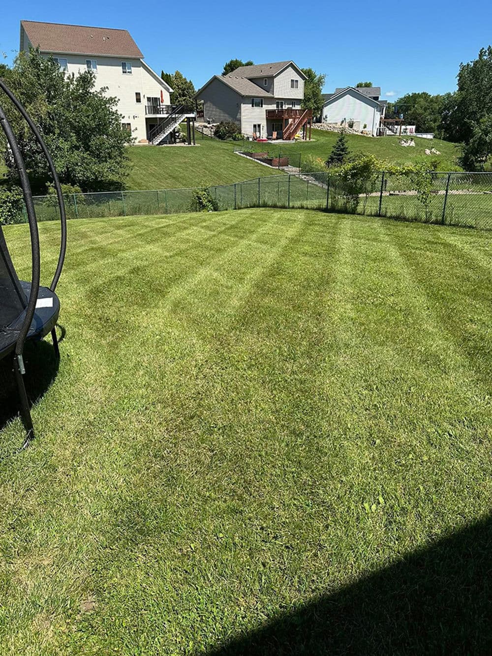 Well-manicured green lawn with a clear blue sky and homes in the background.