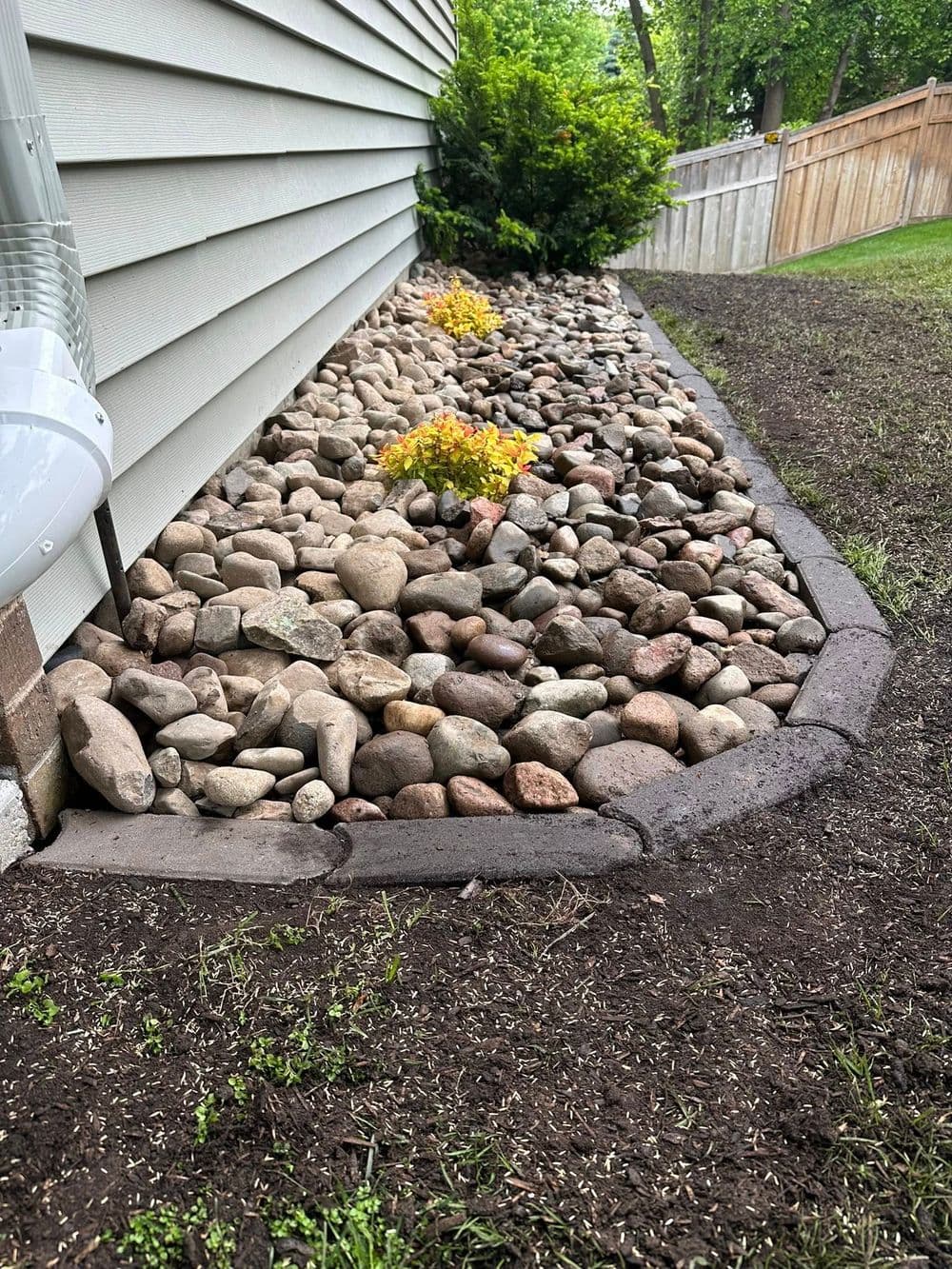 Landscape design featuring river rocks, flowerbed, and a well-maintained garden border.